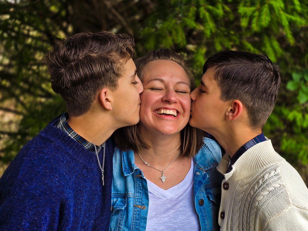 Stephanie laughing as two of her children kiss her cheeks